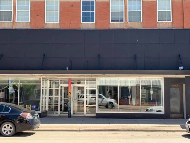 Street view of Barefaced Studio in Grafton, ND, showing an indented glass-door entrance with glass windows on both sides. There is a thick black wall above with checkered white windows intermittently on top.