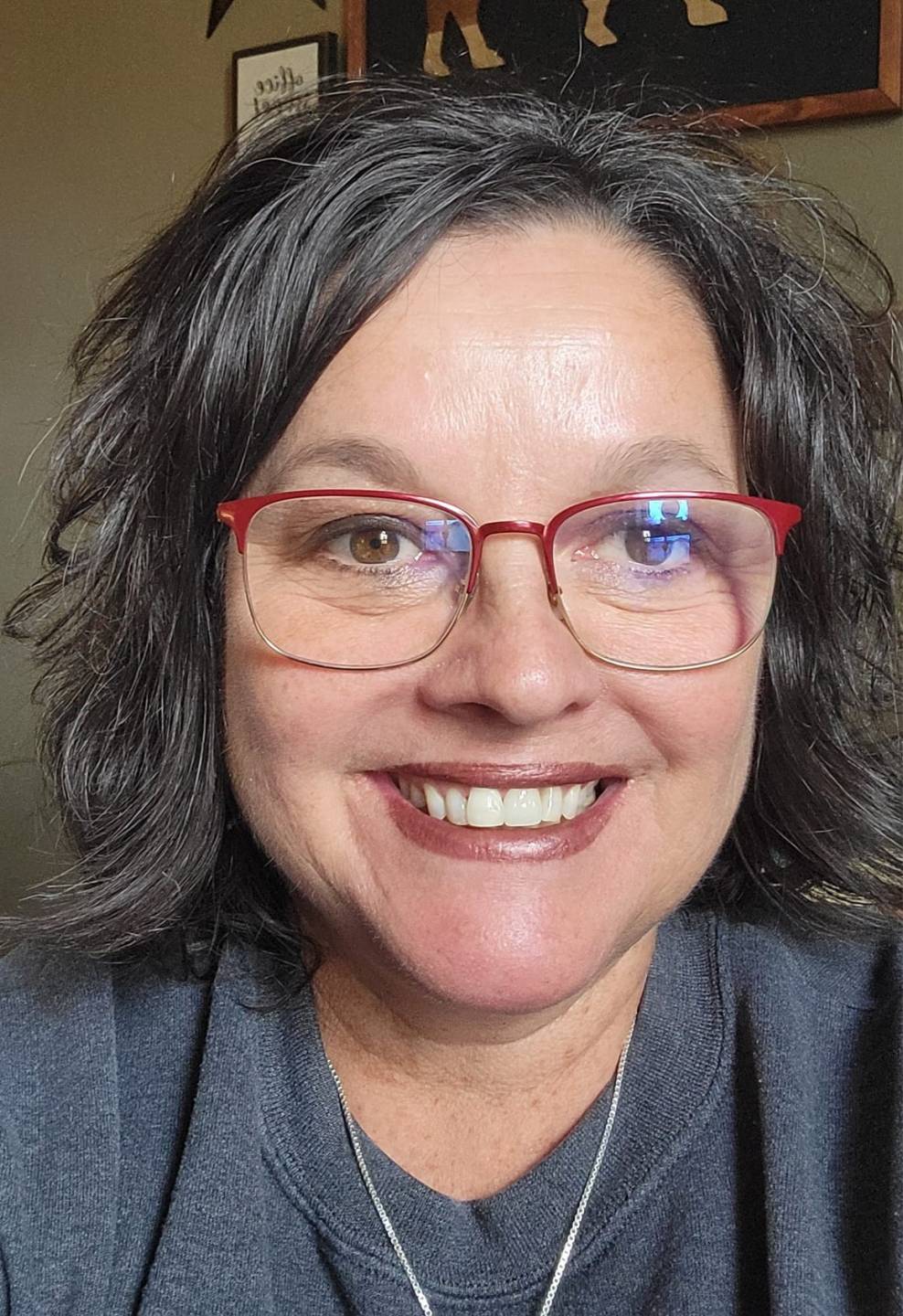 close-up of caucasian Antoinette Heier with shoulder-length, wavy dark hair, thin, red-rimmed glasses, dark brown eyes and a big toothy smile