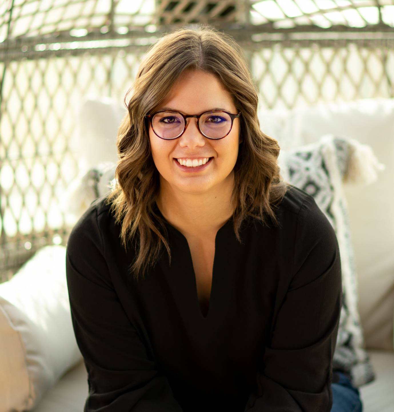 waist-up image of caucasian Brooklyn Engelhart wearing a black long-sleeve shirt, with shoulder-length curly brown hair, wearing round dark-rimmed glasses, with dark eyes and a big toothy smile