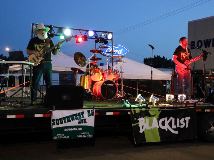 Three people play guitars and drums on stage at night.