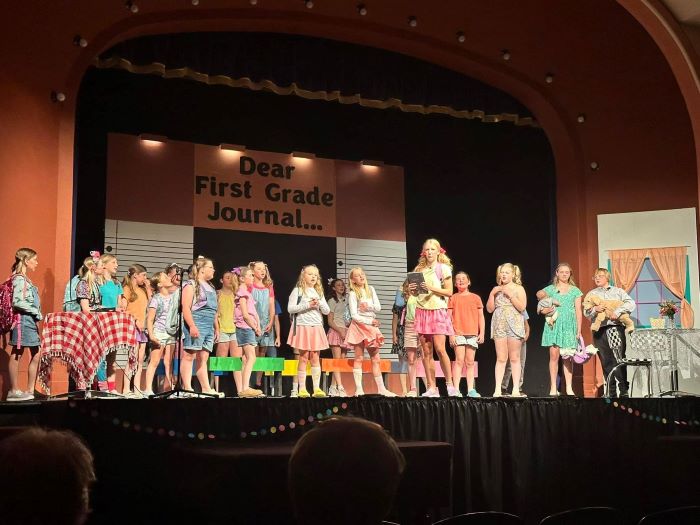 Children in colorful clothes stand on stage and perform a play.