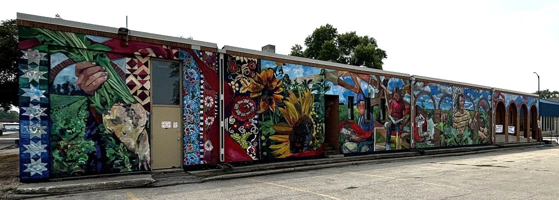 Mural on side of building with flowers, people, sky, and sugar beets.