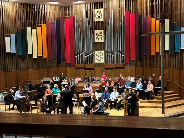 A group of people play instruments underneath a colorful pipe organ.