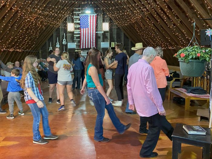 People dance inside a barn, some in a line and some in pairs.