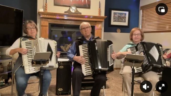 Two women and one man sit with accordions and play music.