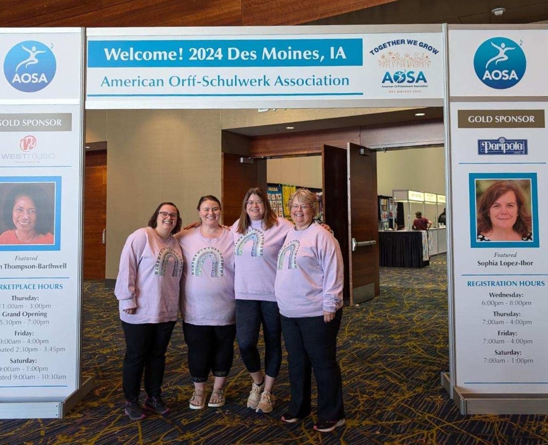 Four women in pink sweatshirts underneath a convention poster.