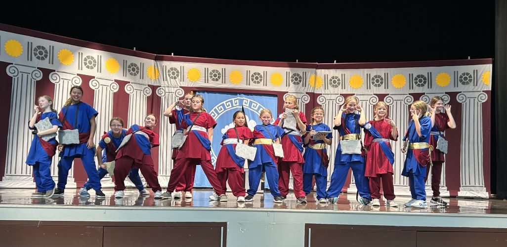 Line of children on stage in blue and red costumes.