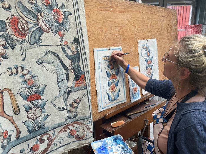 A woman paints flowers next to a painting of a man on horseback.