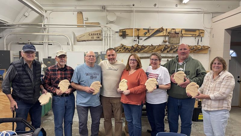 Eight people stand holding wood carvings of eagle heads.