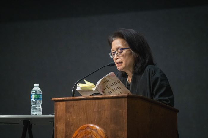 A woman stands behind a podium and reads from her book