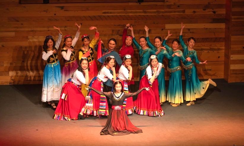 Group of female dancers posing with arms extended, wearing colorful dresses.